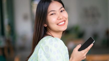 Smiling Asian girl with silky, black hair holding her phone.