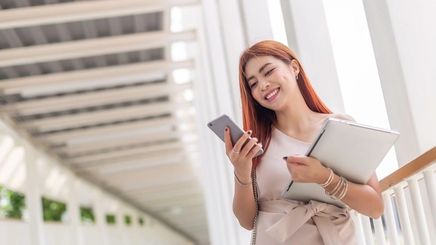 Asian woman with copper hair holding her phone and laptop. 