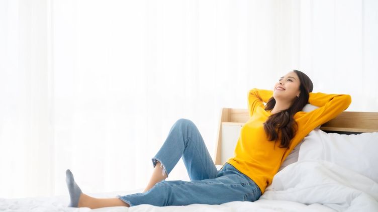 Asian woman in yellow sweater relaxing on white bed