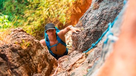 Asian man climbing rocks with blue harness.