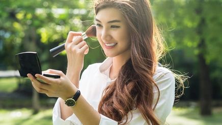 Asian woman applying powder with a brush outdoors.