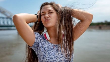 Asian woman scrunching up hair by beach.