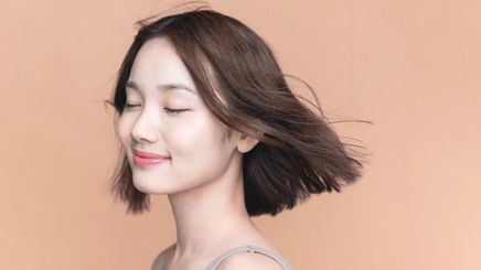 Asian girl with short hair blowing in the wind against brown background