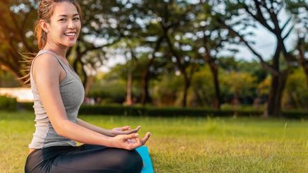 Woman in a meditating position, smiling while outdoors.