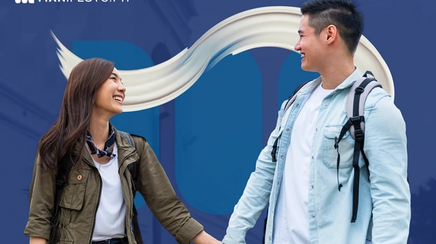 Young Asian couple smiling at each other while holding hands and walking on the street.