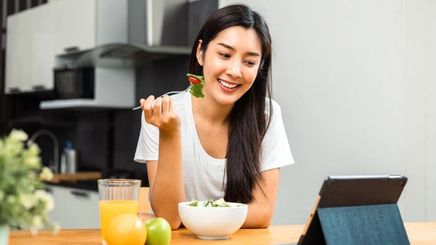 Happy Asian woman eating a salad while watching tablet.