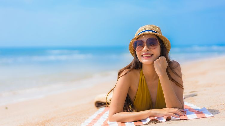 Asian woman wearing a hat and sunglasses while sunbathing on the beach