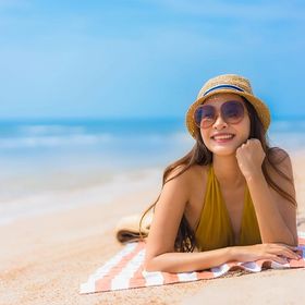 Asian woman wearing a hat and sunglasses while sunbathing on the beach
