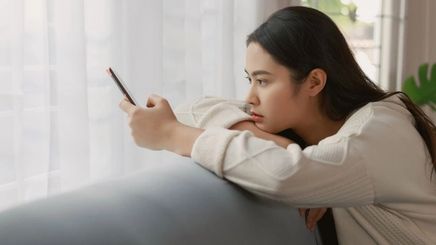 Filipino woman looking sad while using smartphone on couch.