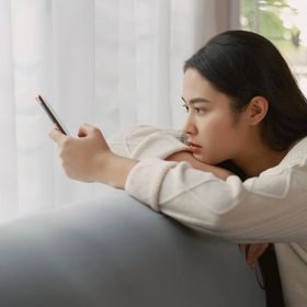 Filipino woman looking sad while using smartphone on couch.
