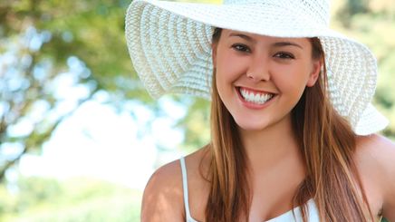 A portrait of smiling woman with white sun hat and tank top.