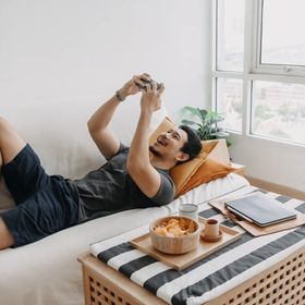 An Asian man playing mobile games while lounging on the sofa.