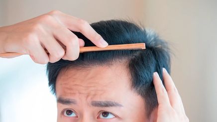 Man brushing his black hair with a wooden comb.