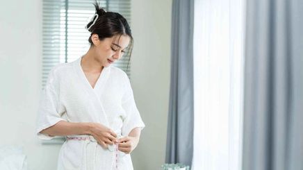 Woman putting on a clean white bathrobe after shower.