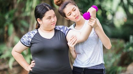 Two Asian friends exercising with a pink dumbbell outdoors 
