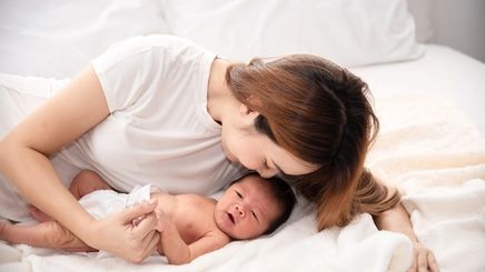 Woman lying on bed with her baby. 