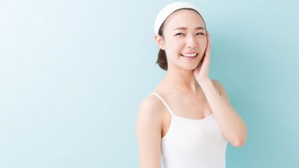A young Asian woman wearing a white tank top and white headband touching her face