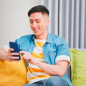 Asian man sitting on a sofa while checking his phone.