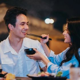 Asian woman feeding man with chopsticks.