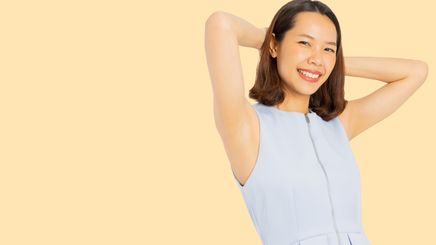 An Asian woman in blue peplum top with arms raised and hands touching her head