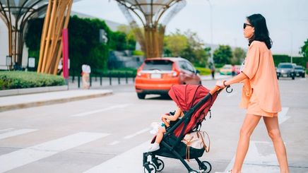Asian woman in coordinates pushing baby stroller outdoors.