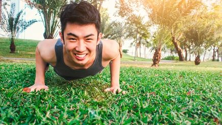 Young Asian male performs a push-up at a park.