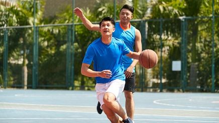 Two Asian men playing basketball outdoors