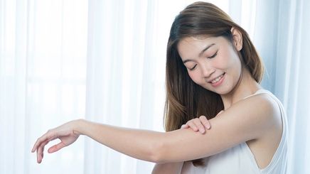 Asian woman applying lotion on arm