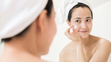 Asian woman applying pimple treatment on her cheek.