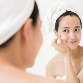 Asian woman applying pimple treatment on her cheek.