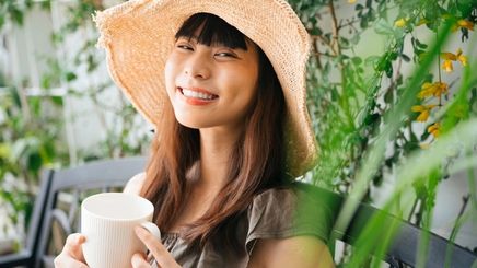 Woman with a straw hat holding a cup and smiling at the camera.