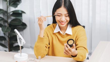 Smiling woman applying eyeshadow with a brush on her eyelid.