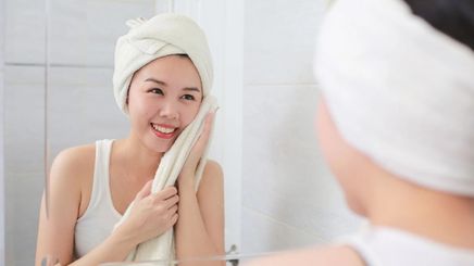 An Asian woman smiling and wiping her face with a towel