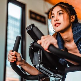 Asian woman hunched on exercise bike.