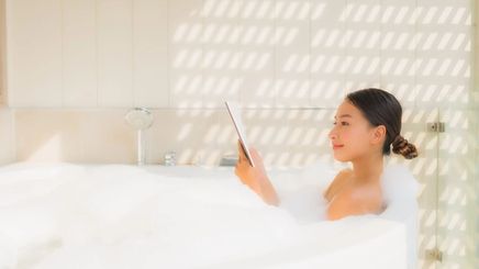 Asian woman happily applying skincare during her self-care time.