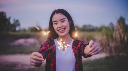 Asian woman in red plaid shirt holding sparkler in the outdoors.