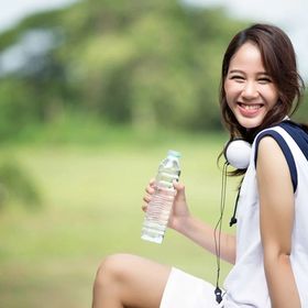 Asian woman smiling holding a bottle of water and exercising outdoors. 