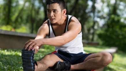 Young Asian man doing leg stretches in the park