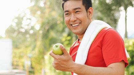 A man smiling after a run while holding an apple.