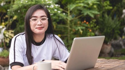 An Asian with glasses and pimples typing on a laptop outdoors
