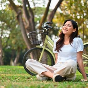 Asian woman in white sitting on bike on grass.