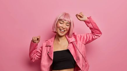 A woman with pink hair wearing a pink jacket and dancing