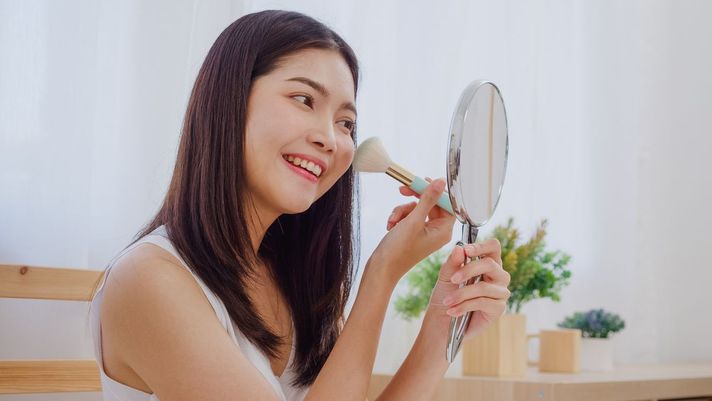 Asian woman applying makeup with fluffy brush 