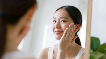 Filipino woman using serum on her face in mirror.