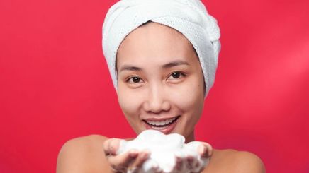 Asian woman holding soap with towel on hair 
