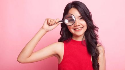 Asian woman in red top holding a magnifying glass
