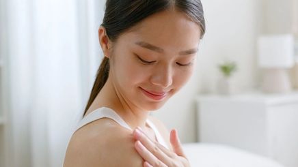 Asian woman applying lotion on her shoulder.