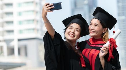 Two Asian girls in a toga taking a photo.