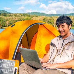 Asian man working on laptop while camping.