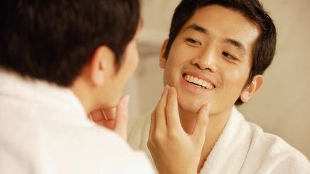 Young man touching his face while looking at the mirror